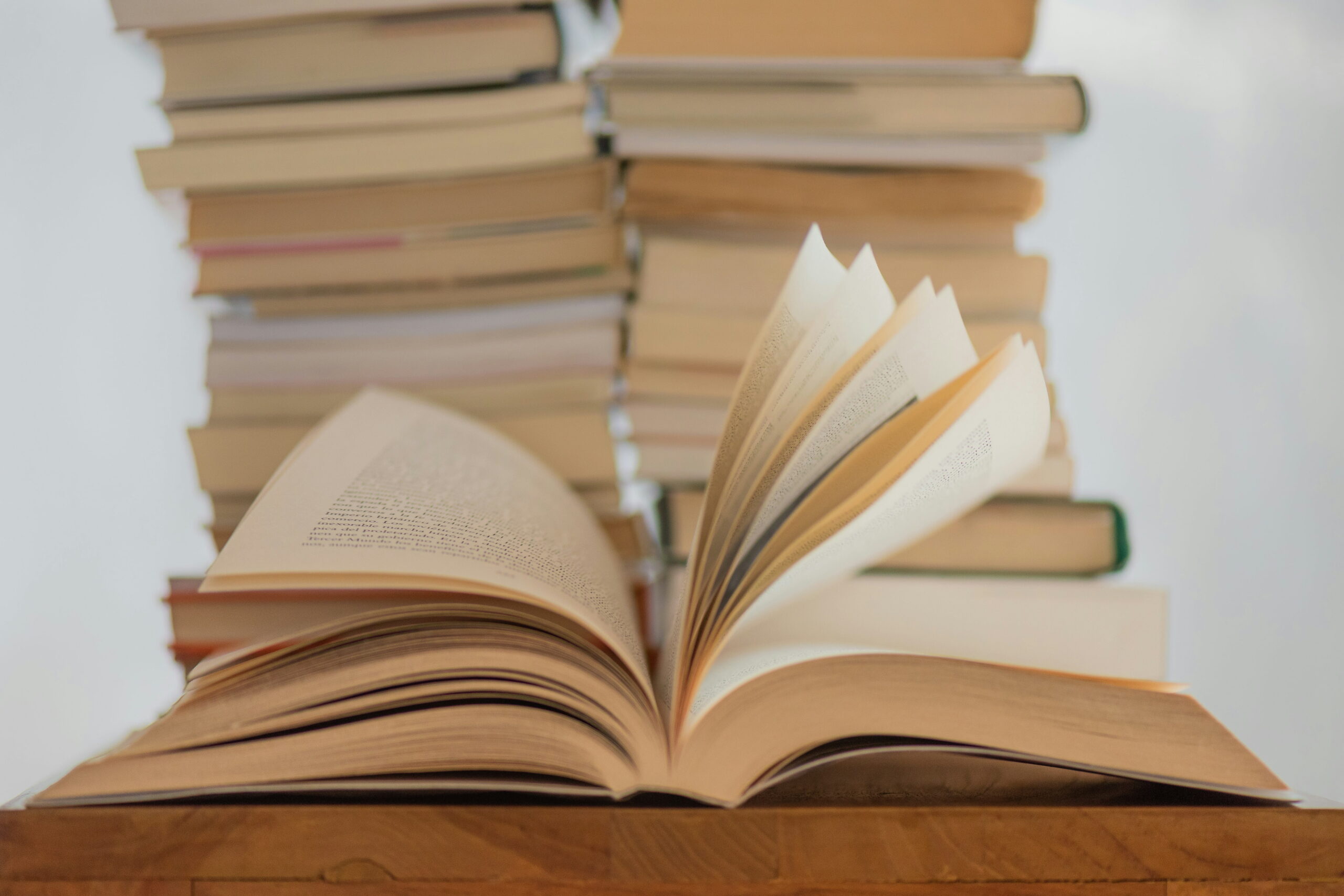 An open book sits in the foreground with its pages dynamically flipping, set against a blurred background of tall vertical stacks of books.