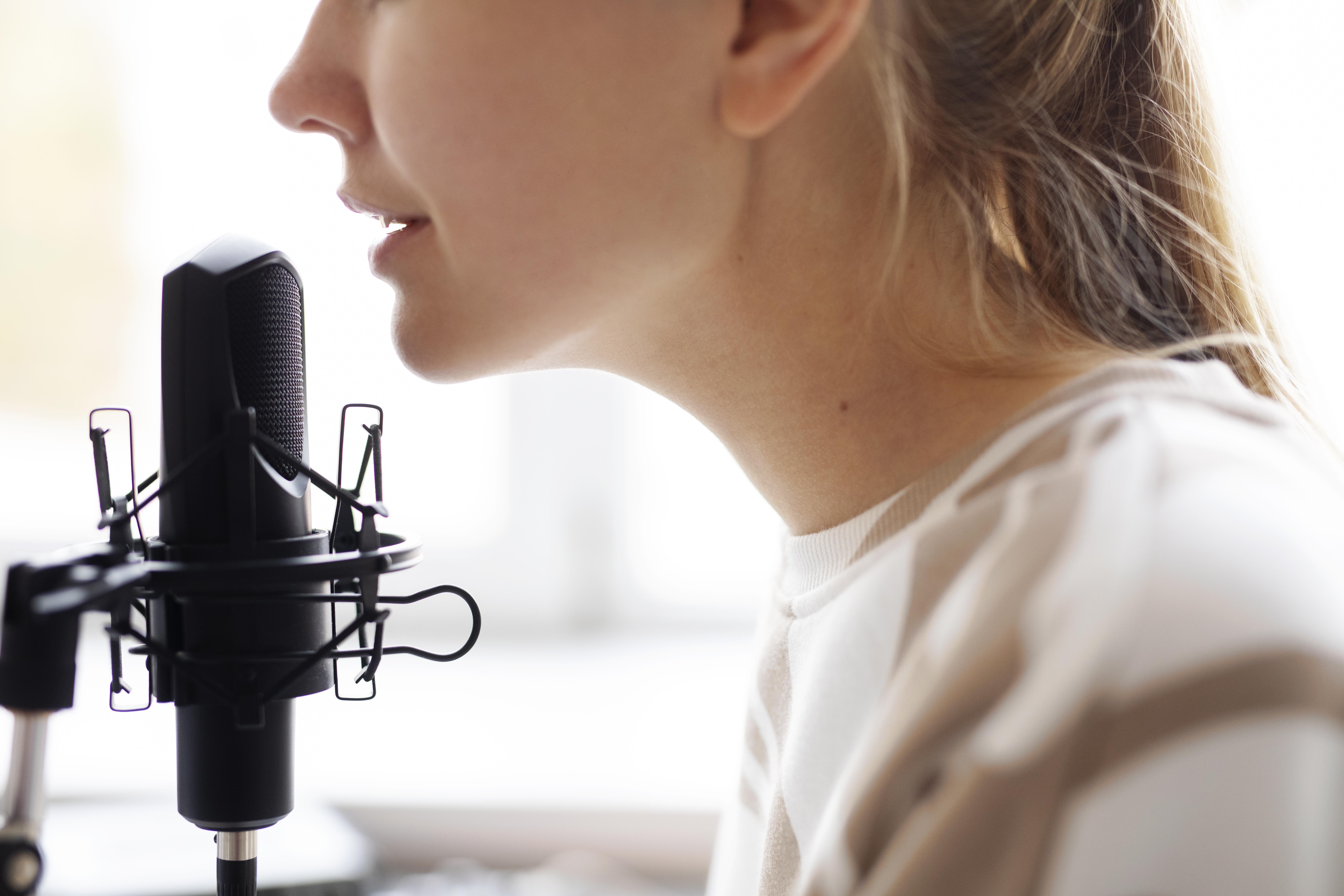 Side profile close-up of a woman speaking close into a professional black studio microphone mounted in a shock mount.
