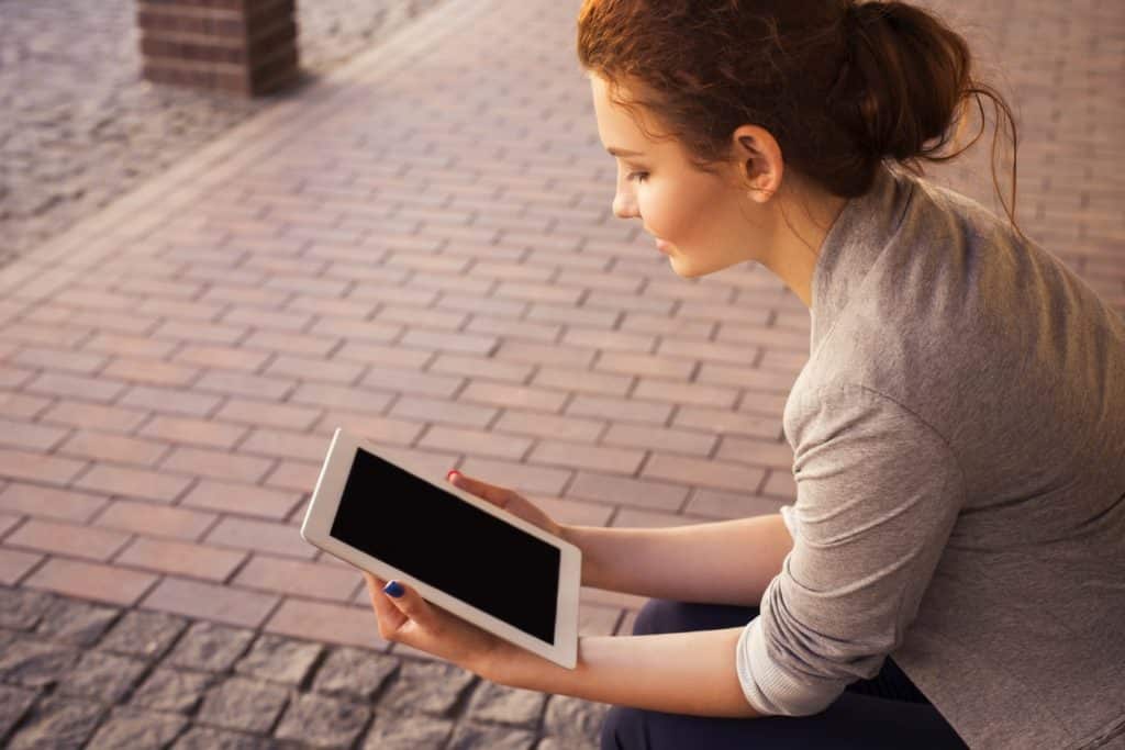 Woman sitting on the sidewalk looking at a tablet