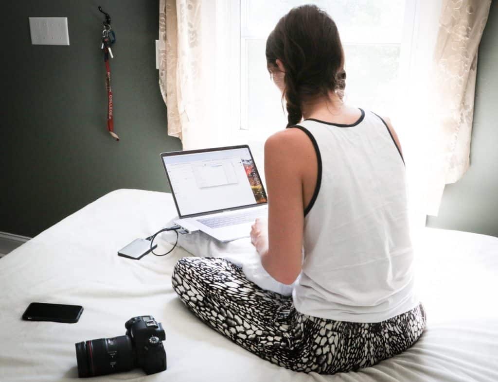 woman working on her laptop, camera and mobile phone on a bed