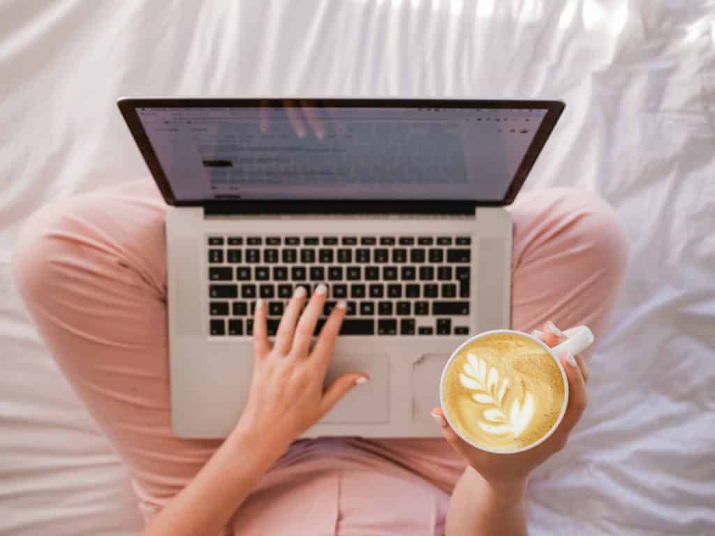person with a laptop on her lap, holding a cup of coffee