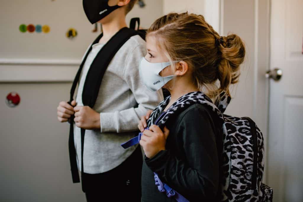 2 children wearing a backpack with facemasks on