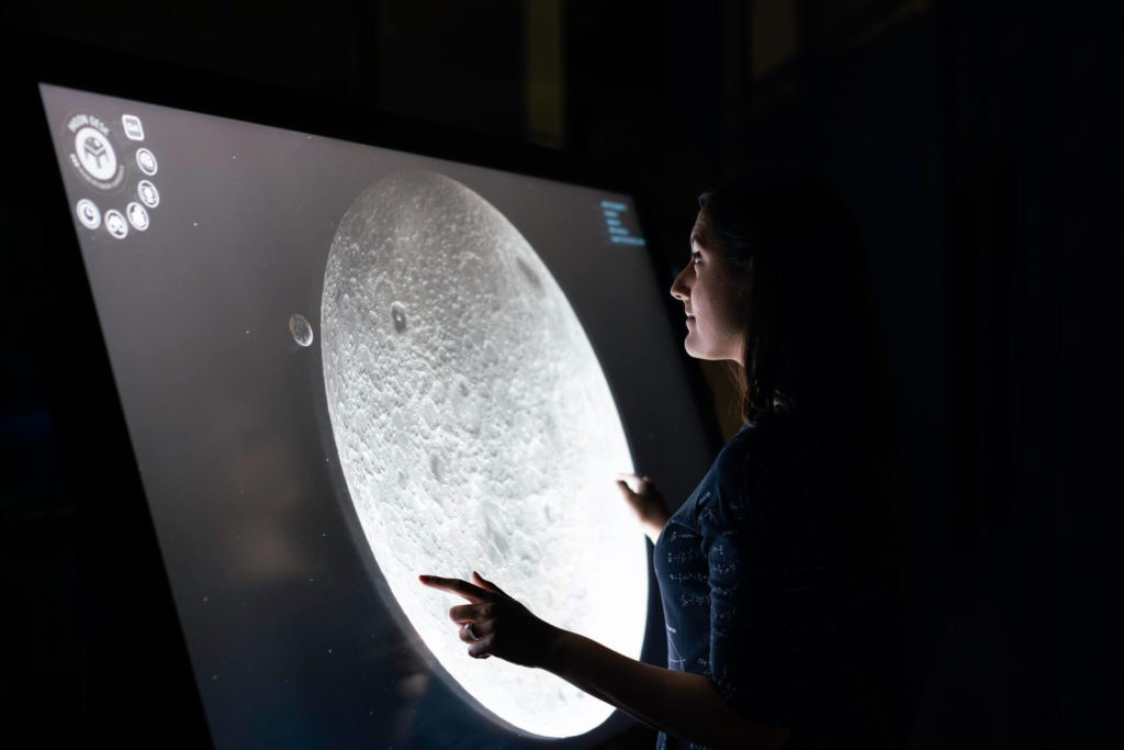 person in front of a big screen displaying an image of the moon