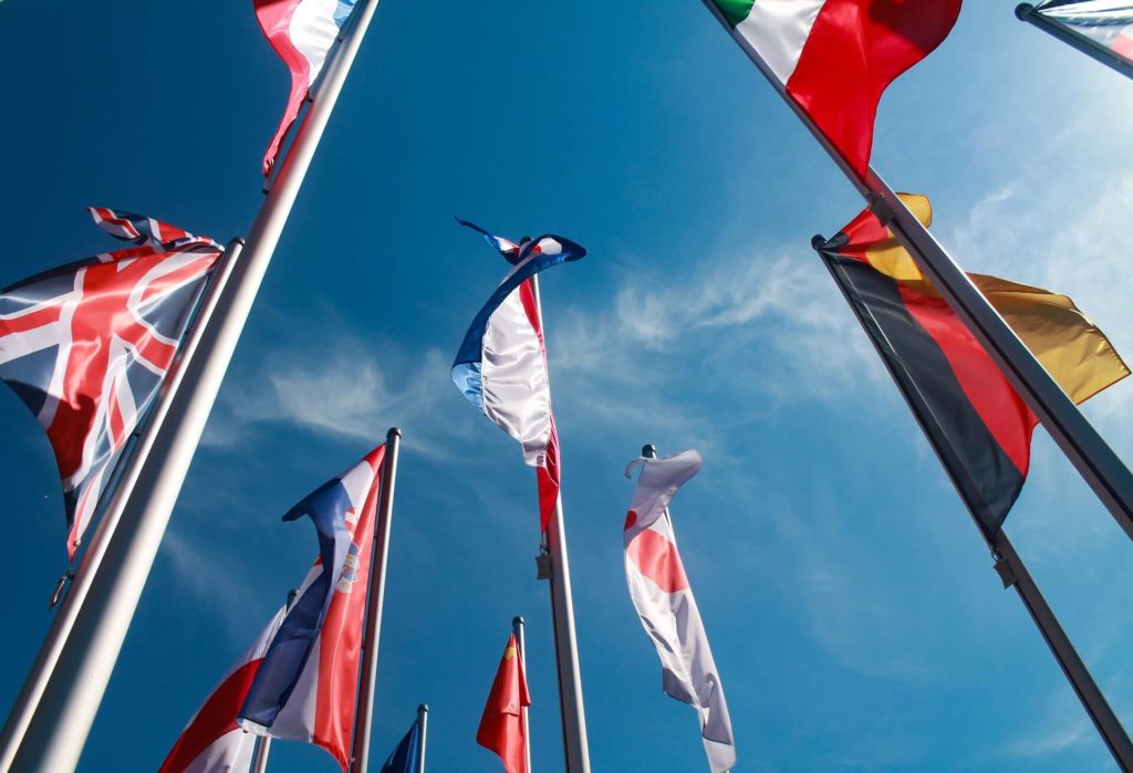 view from below of flags of different countries, situated on poles