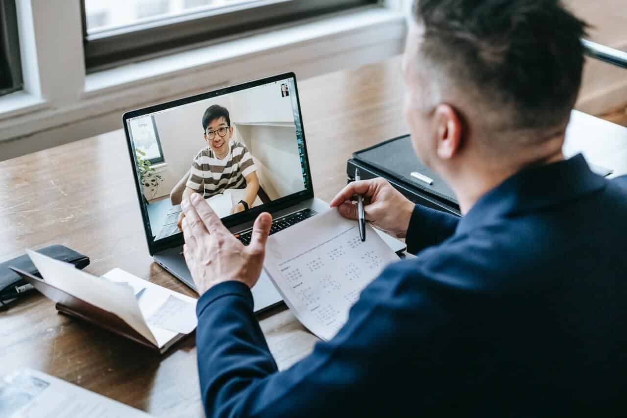 man in a video call on his laptop, with books and documents on the table