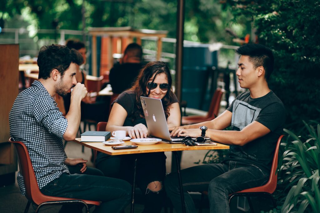 three people speaking to each other and looking at computers in a cafe