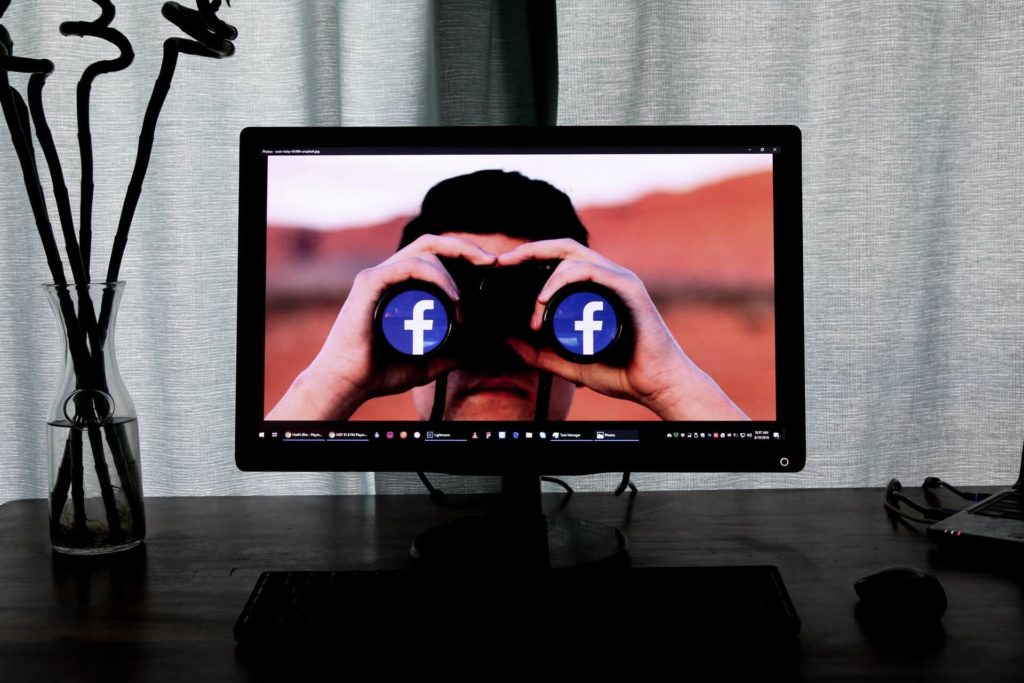 monitor showing a person looking in a binocular with facebook logo