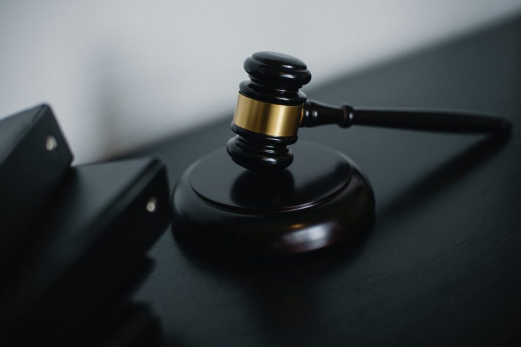Based on the provided image, it shows a judge's gavel with a metallic gold band resting on its sounding block next to a dark folder or binder.