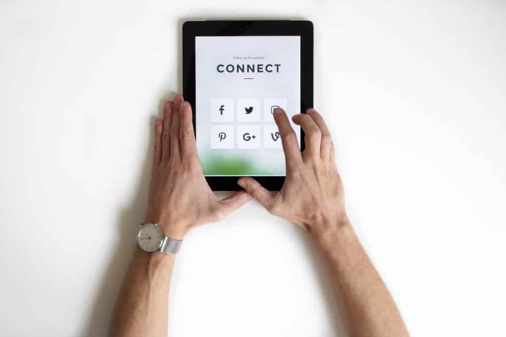 A set of hands holding a tablet that is showing different social media platform icon.