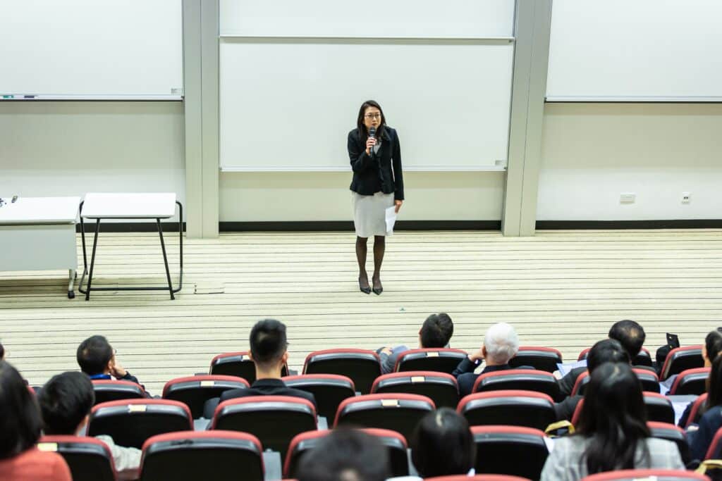 A woman giving a talk in front of a university classroom.