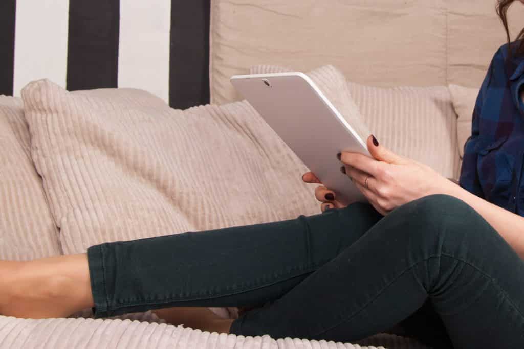 A woman sitting on the couch while using a tablet.