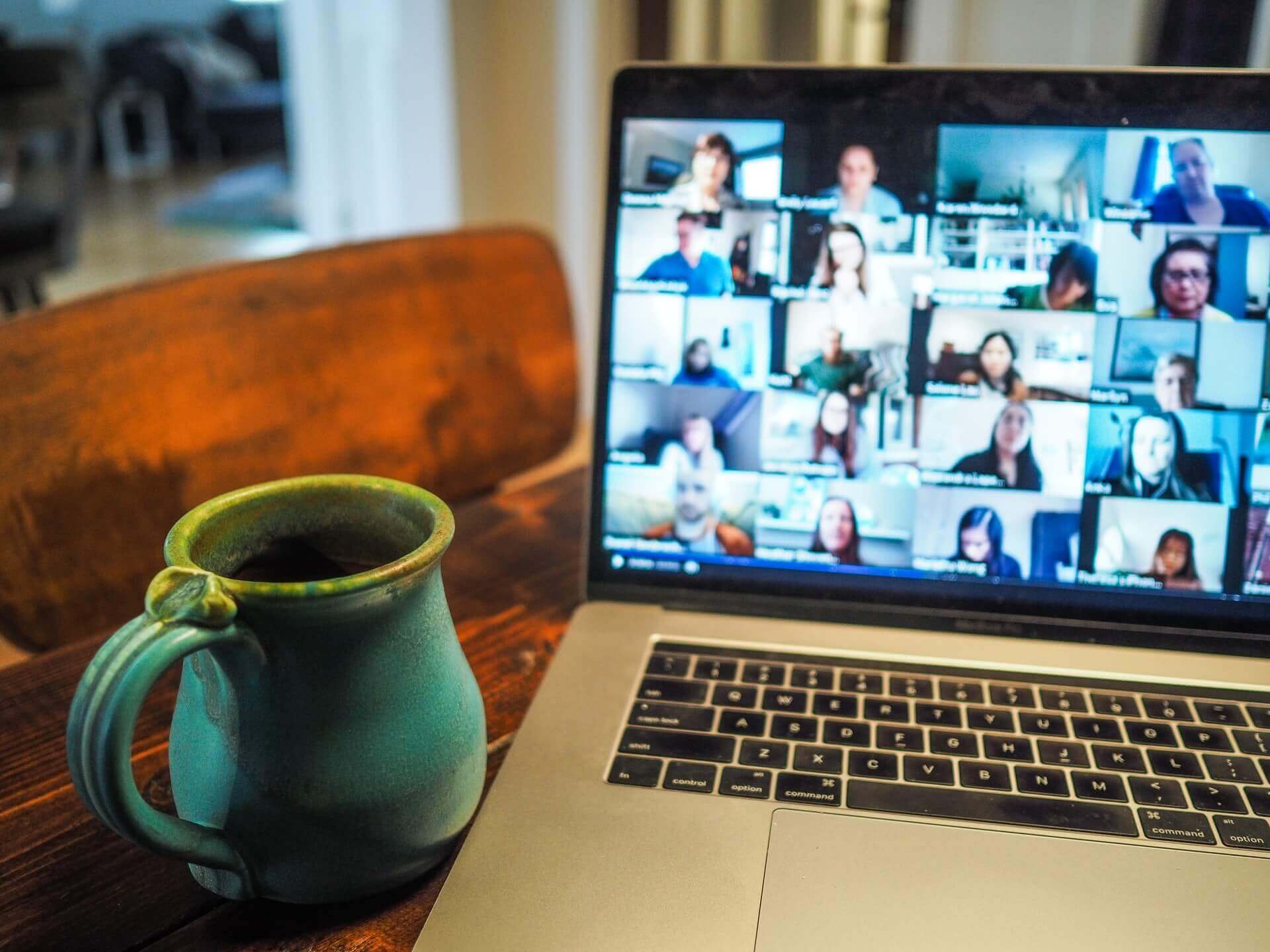 A laptop used for online meeting is placed beside a mug on the table