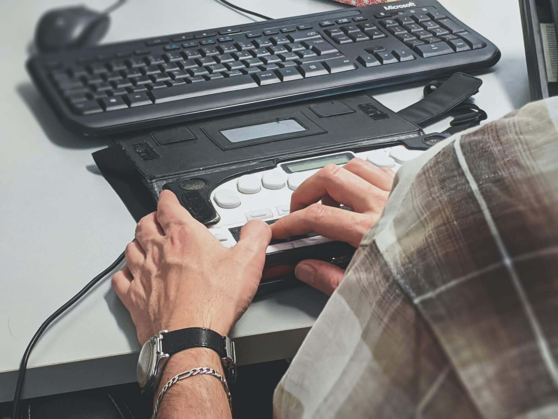 A man using a stenograph machine beside a keyboard