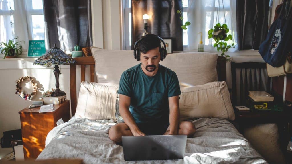 a man with headset sitting on the bed while using a laptop