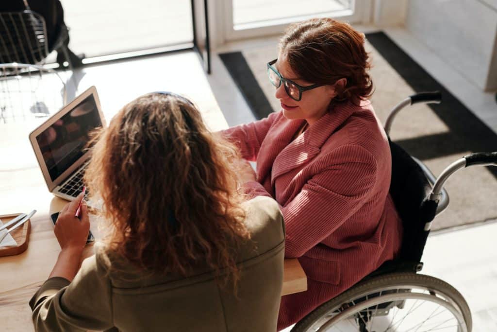 two women conducting a meeting and one of them is sitting on a wheelchair 