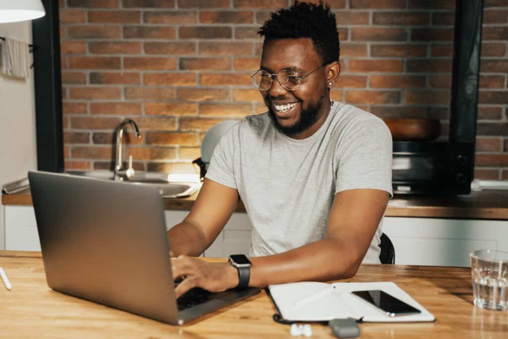 a man smiling while using his laptop that is placed on island kitchen top