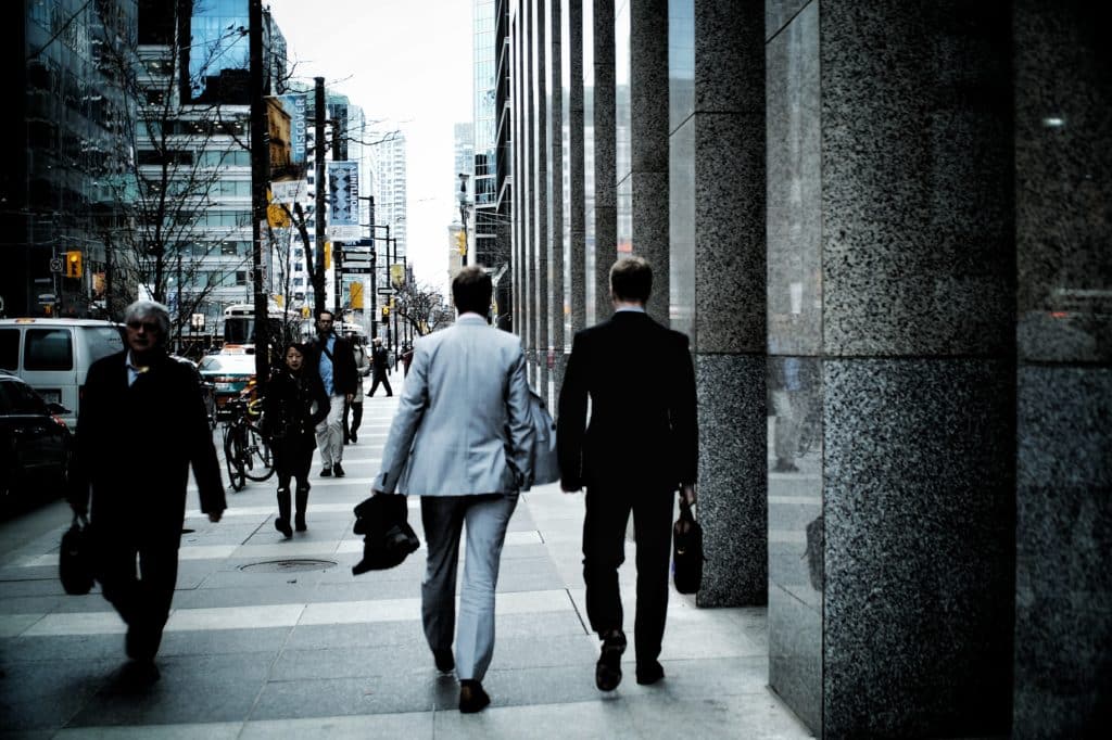 Sidewalk with focus on 2 men in suit walking near a building