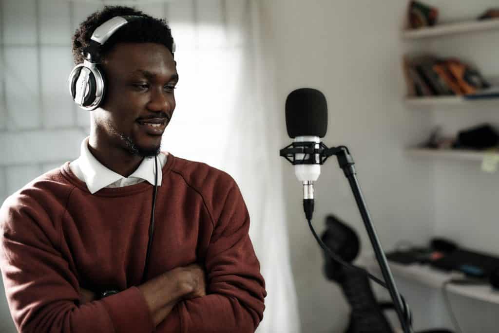 Man in a sweater and headphones speaking into a microphone