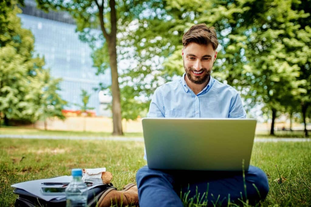 smiling person sitting on the grass working on his laptop
