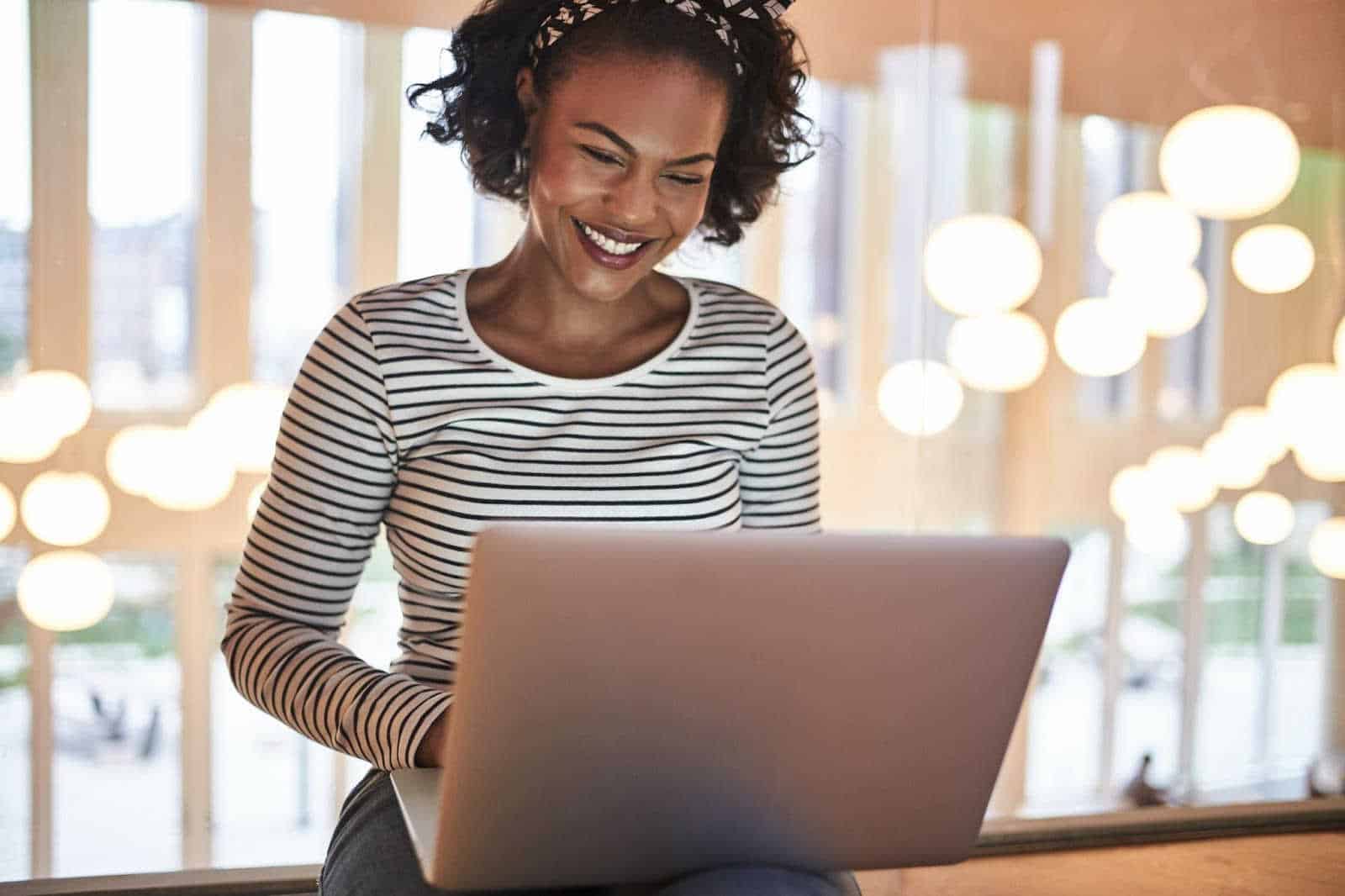 smiling woman looking at her laptop placed on her lap