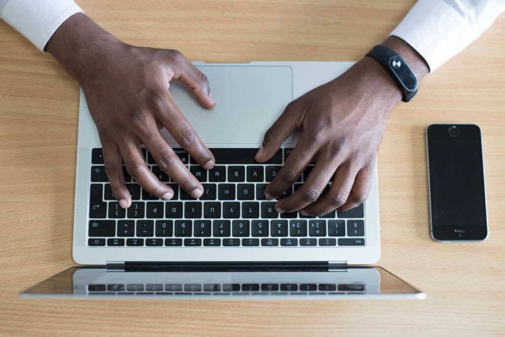 hands typing on a laptop with a mobile phone on the table