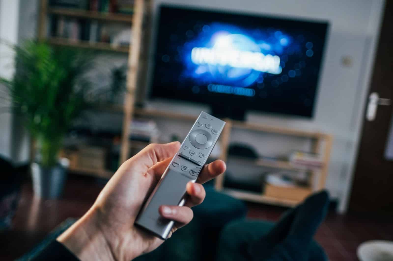 a hand holding a remote for the tv in the background