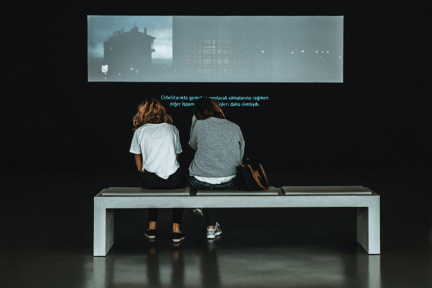 two persons facing a big screen sitting on a bench