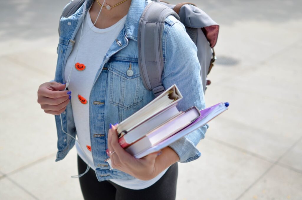 Girl with denim jacket wearing a backpack and carrying books