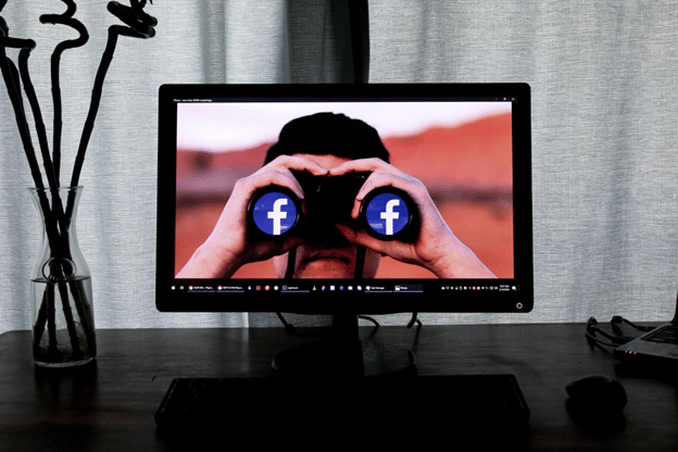 monitor on a table displaying a man holding binoculars with facebook logos on the lens and facebook closed captioning