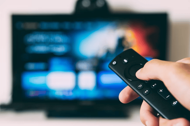 A remote control being held in front of a television