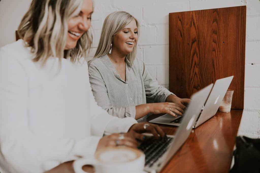 two women working on each of their laptops smiling