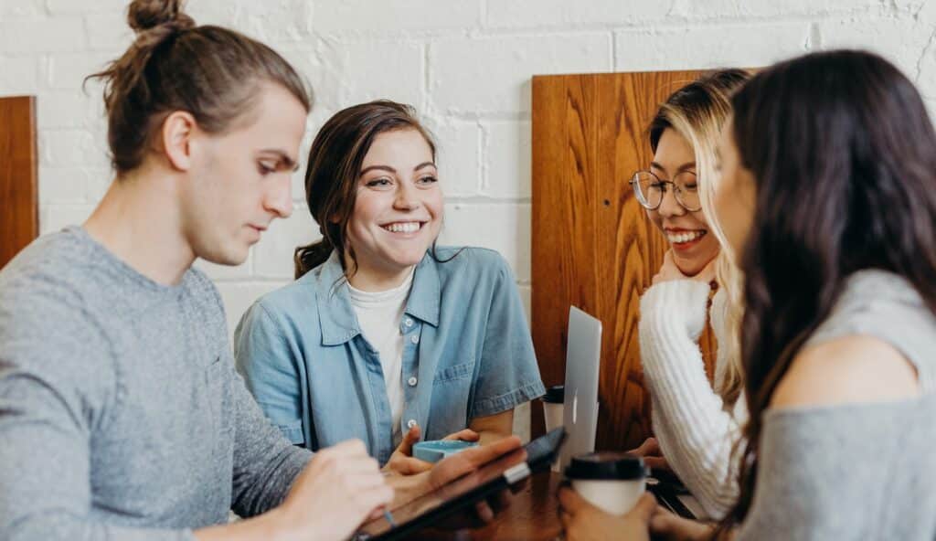 Three women and a man smile and chat while working at a table