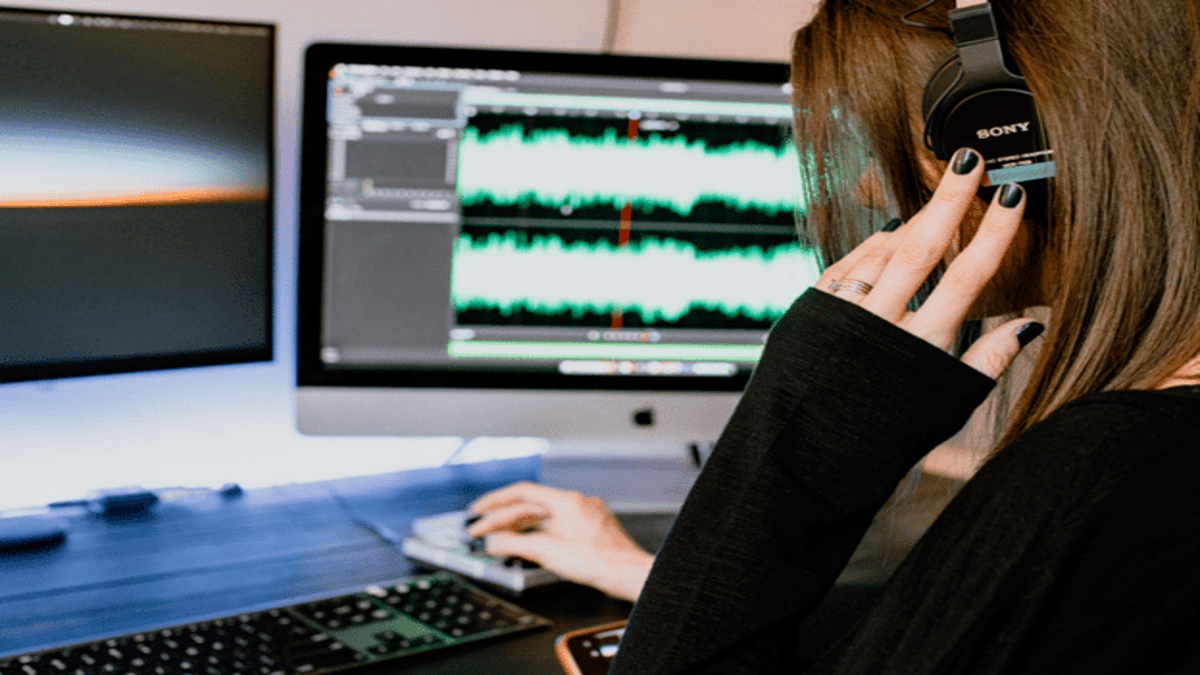 a person with headphones on andworking on an audio software on a computer