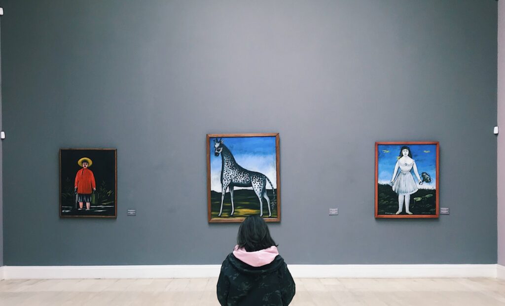 The back of a person as they view paintings in a museum
