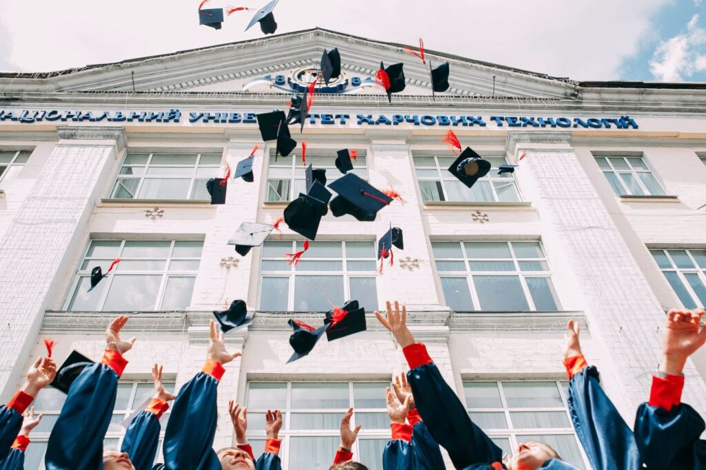 students throwing their graduation cap in front of a school building