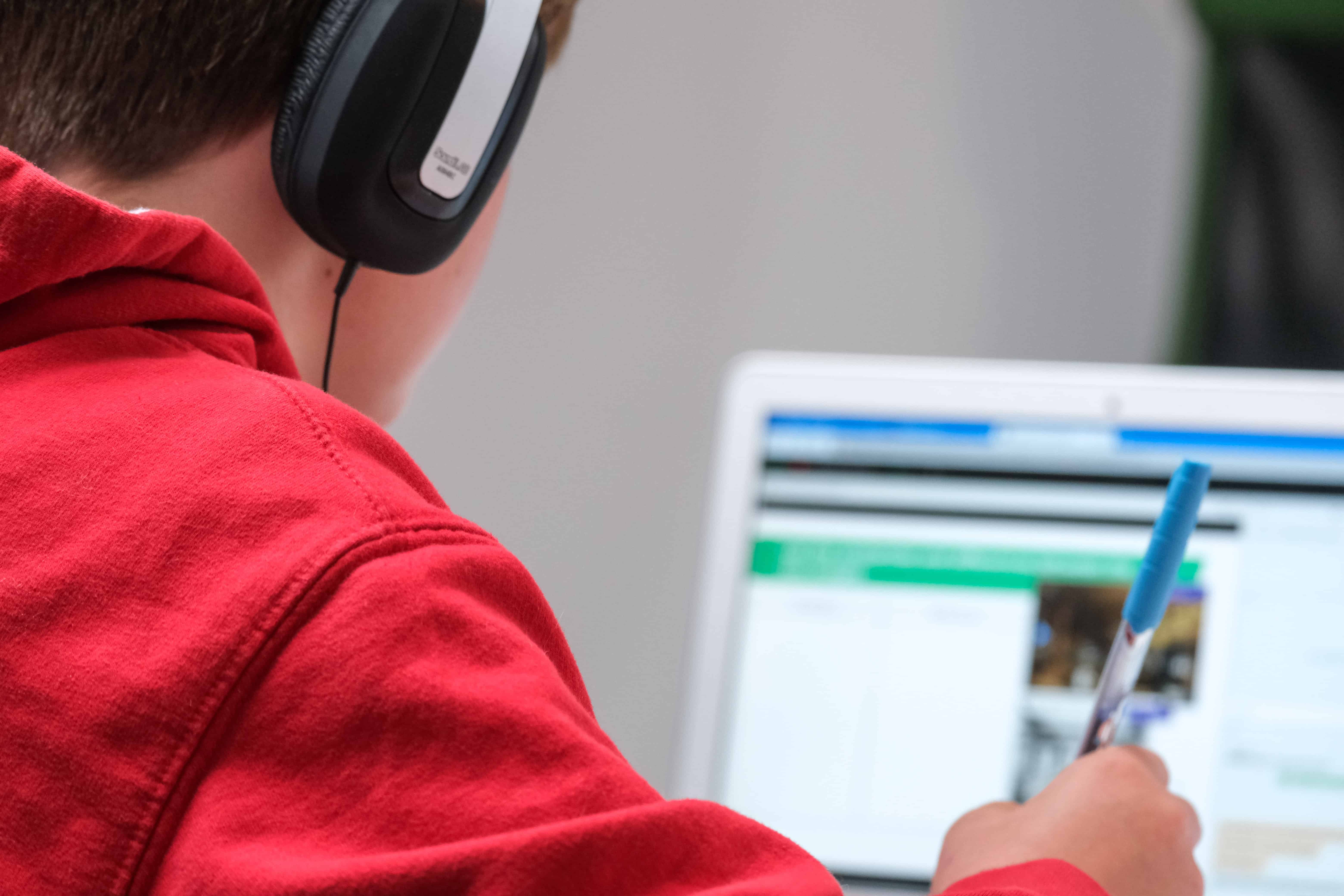 person in a red hoodie wearing headphones in front of a laptop