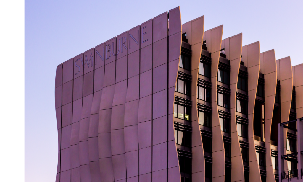 Modern architectural building at Swinburne University of Technology featuring a curved metal facade with vertical panels and large windows, photographed at dusk under a purple sky.