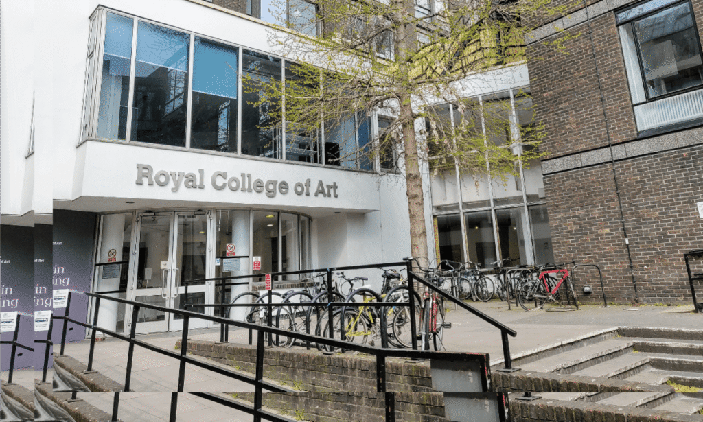 Exterior view of the Royal College of Art building with modern glass and brick architecture, bicycle racks near the entrance, and a tree with fresh spring leaves.