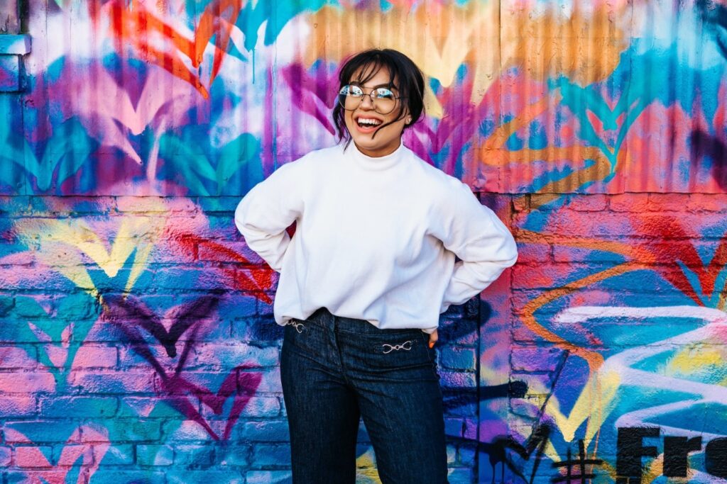 Woman wearing glasses and smiling in front of a bright colored wall