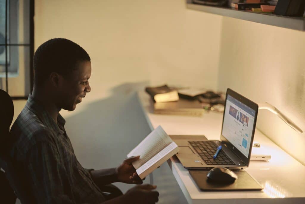 man sitting in front of a laptop reading a book