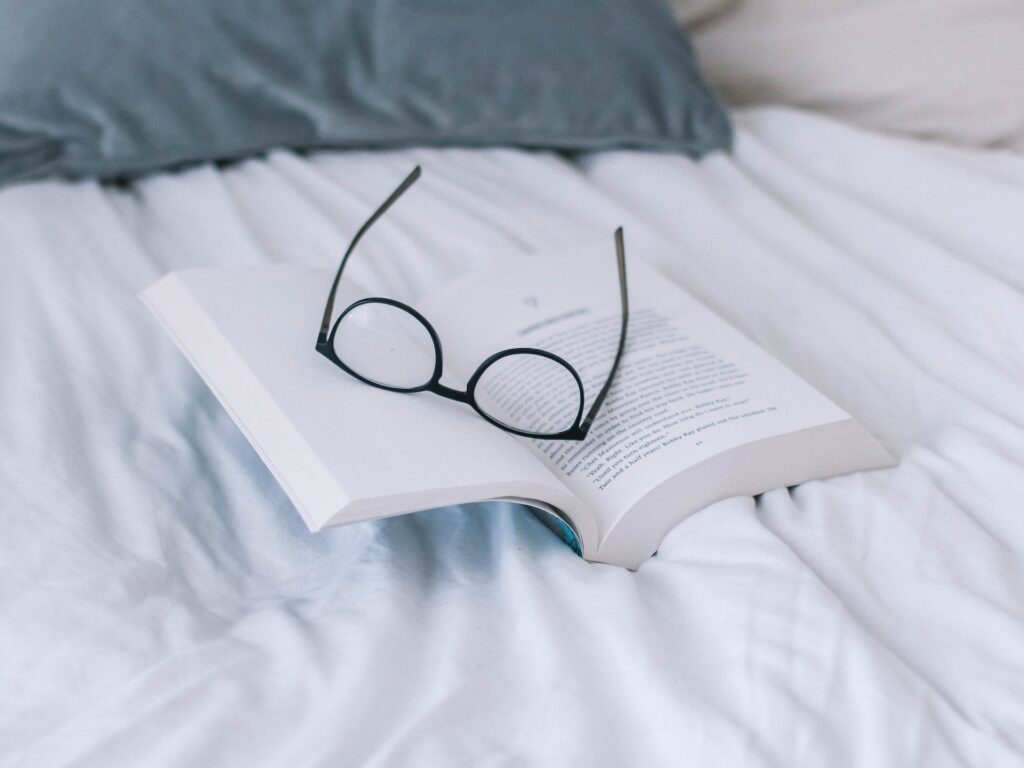 A book with glasses on it on a bed