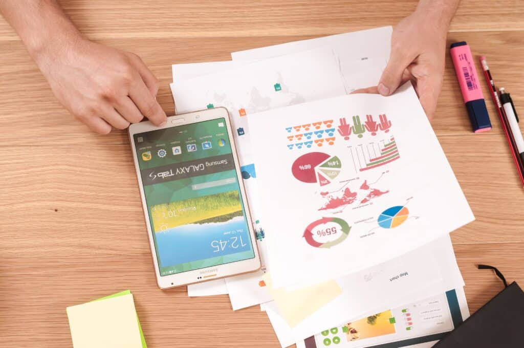 top view of a table with tablet being held by a person's hands and paper with graphs