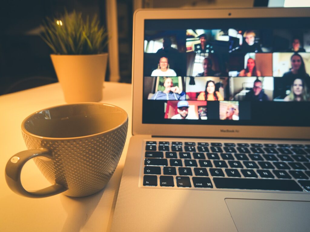 a computer with a video conference call on the screen next to a coffee cup