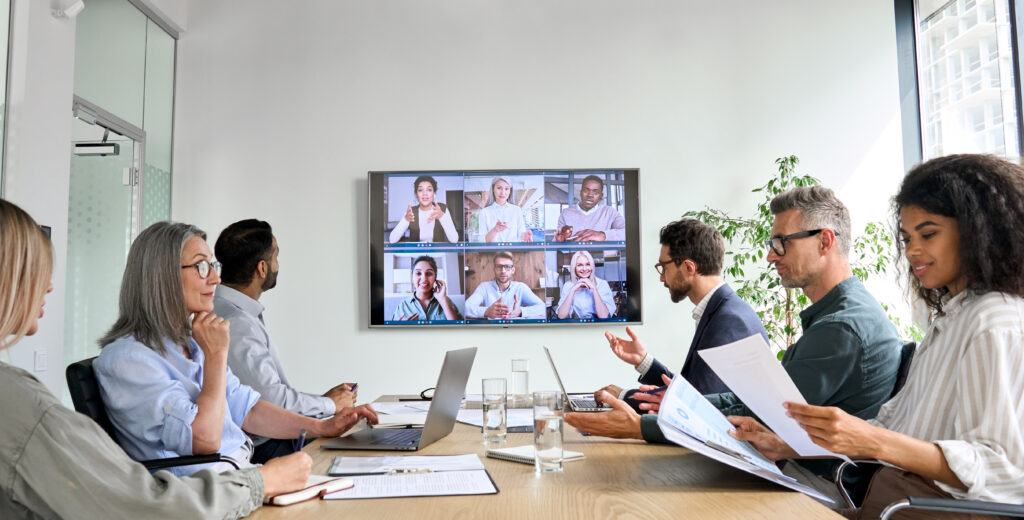 A group of people in a meeting with more participants tuning in remotely