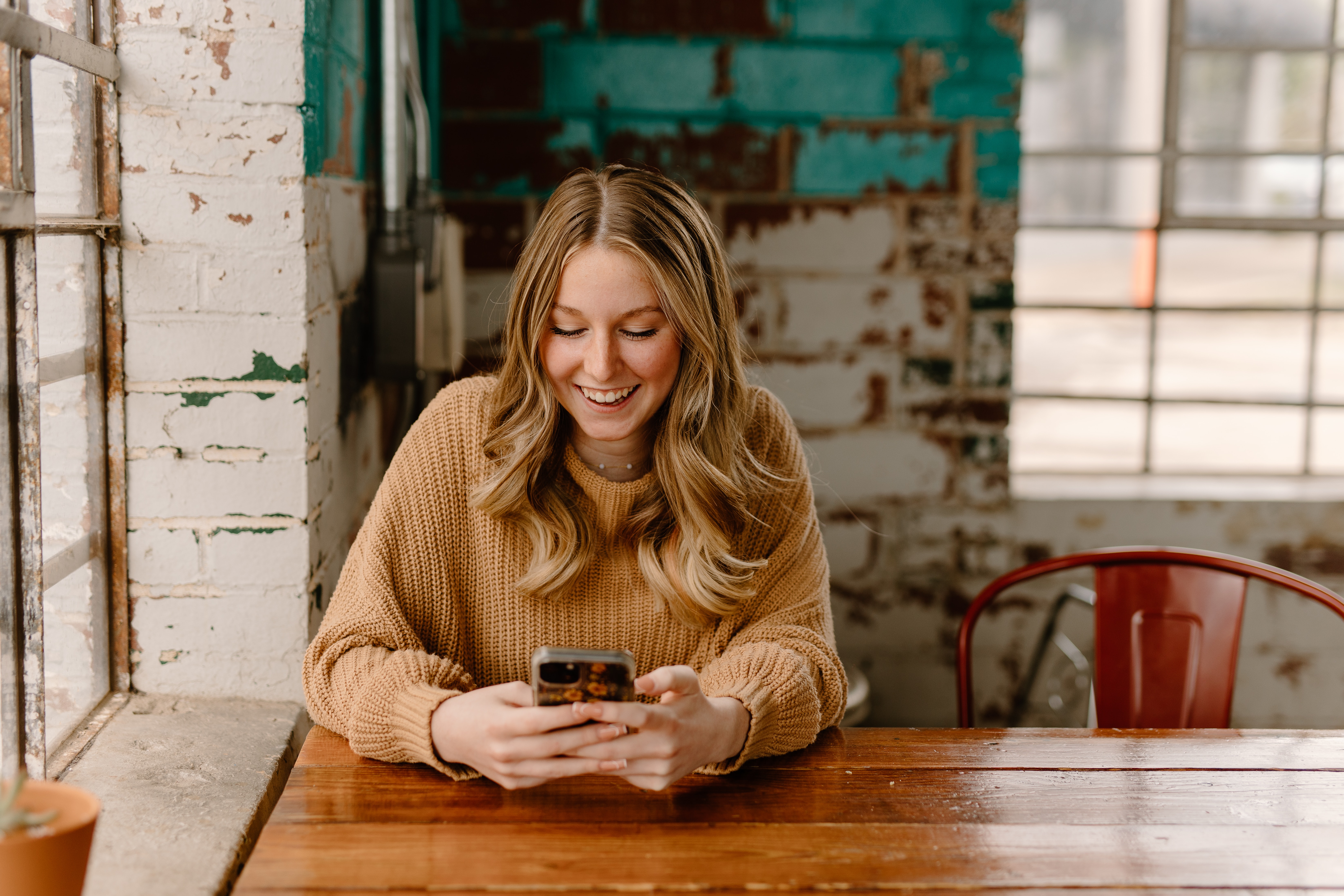 Blonde woman sits at a wooden table and messages on her phone.