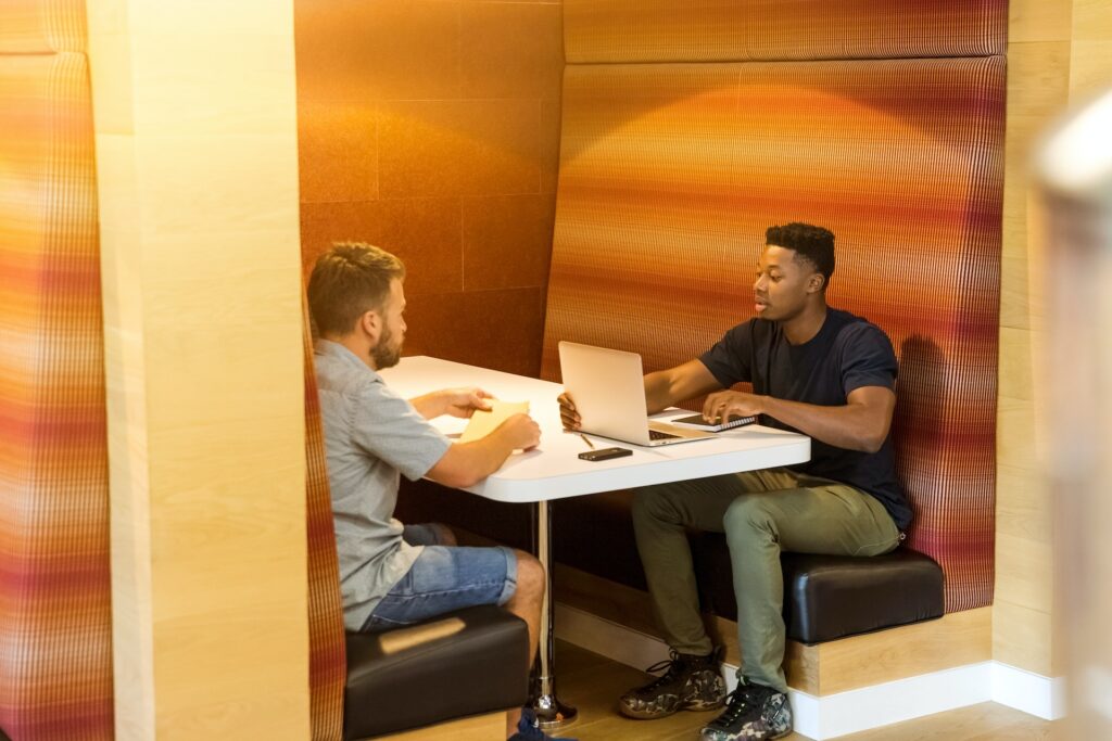 Two men speaking in a booth with a computer