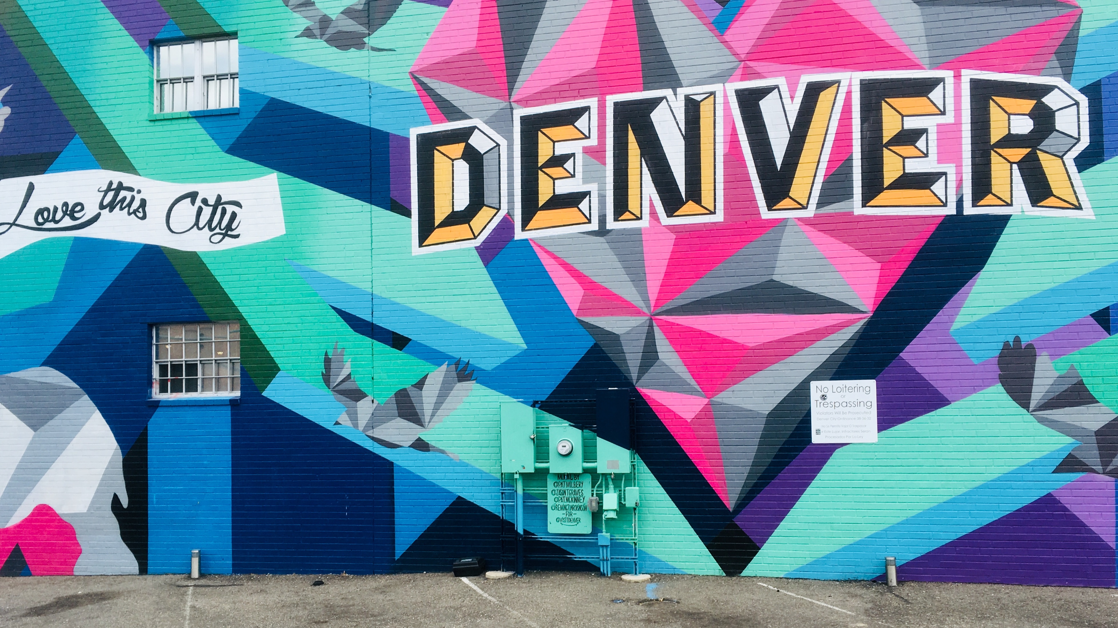 A wall in Denver which has colorful artful graffiti is shown reading ‘Love this city’ in white and ‘DENVER’ in big block black and yellow letters