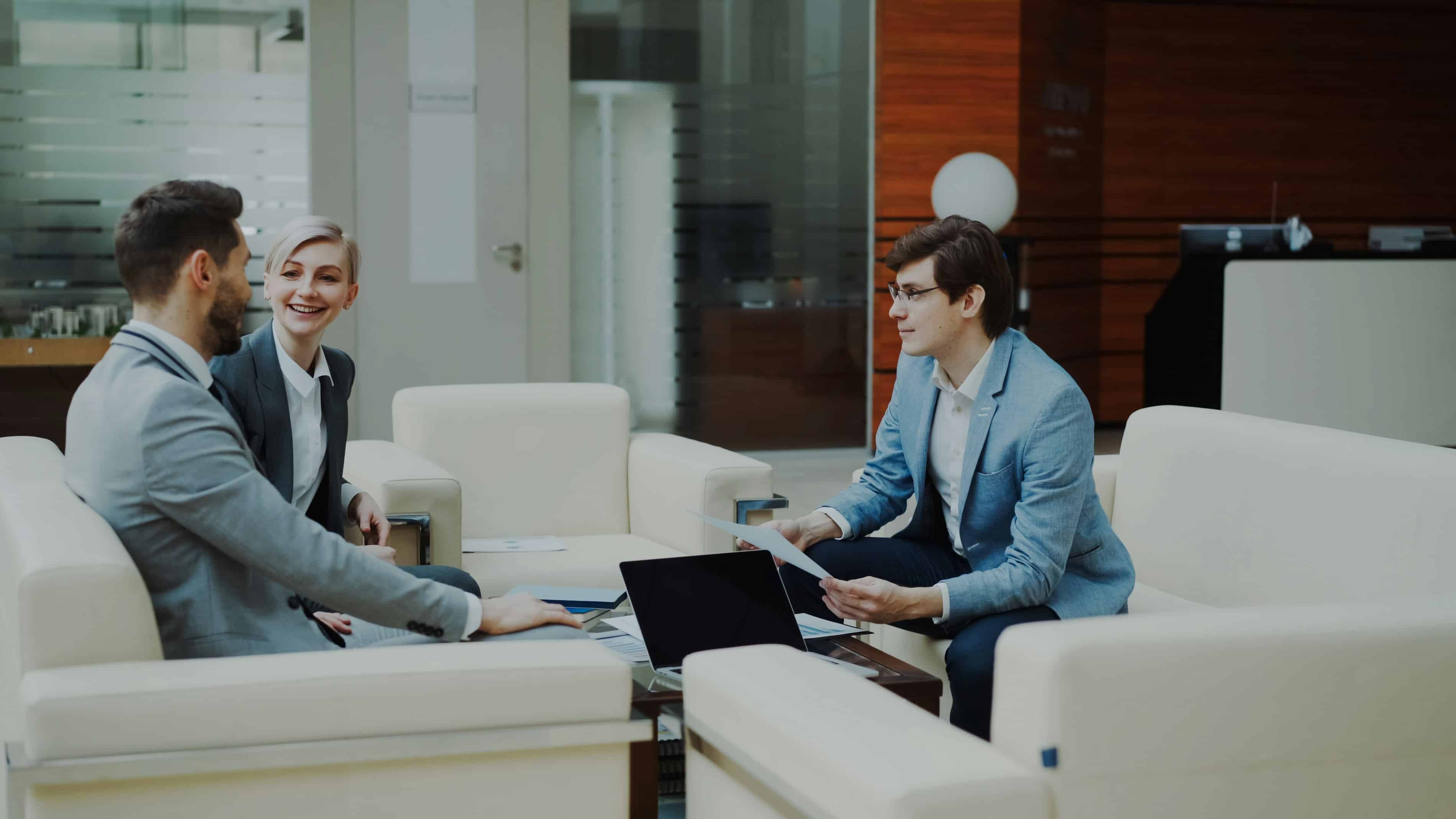 A group of three professionals sit on white couches while in an informal meeting