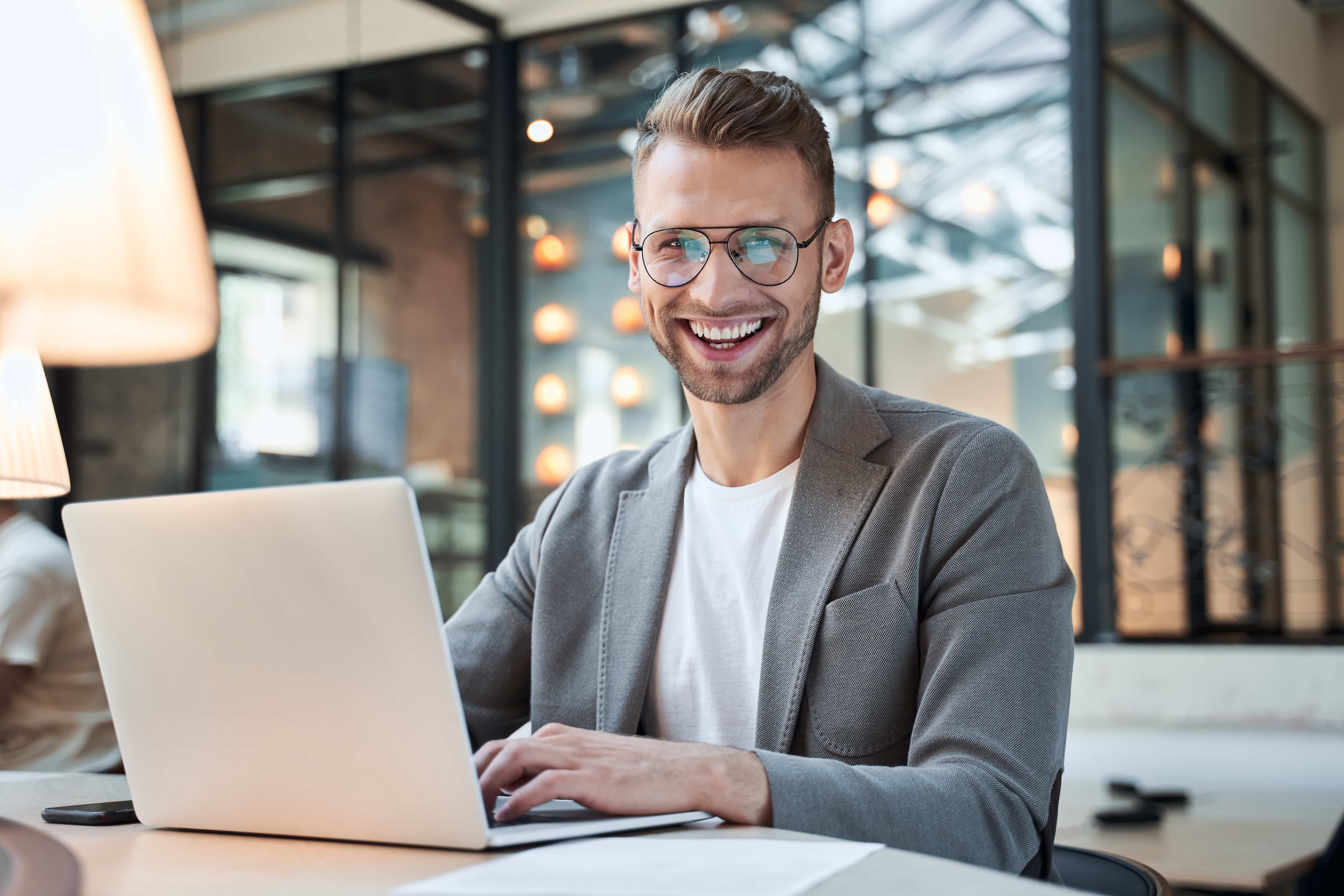 man wearing glasses smiling while working on a computer