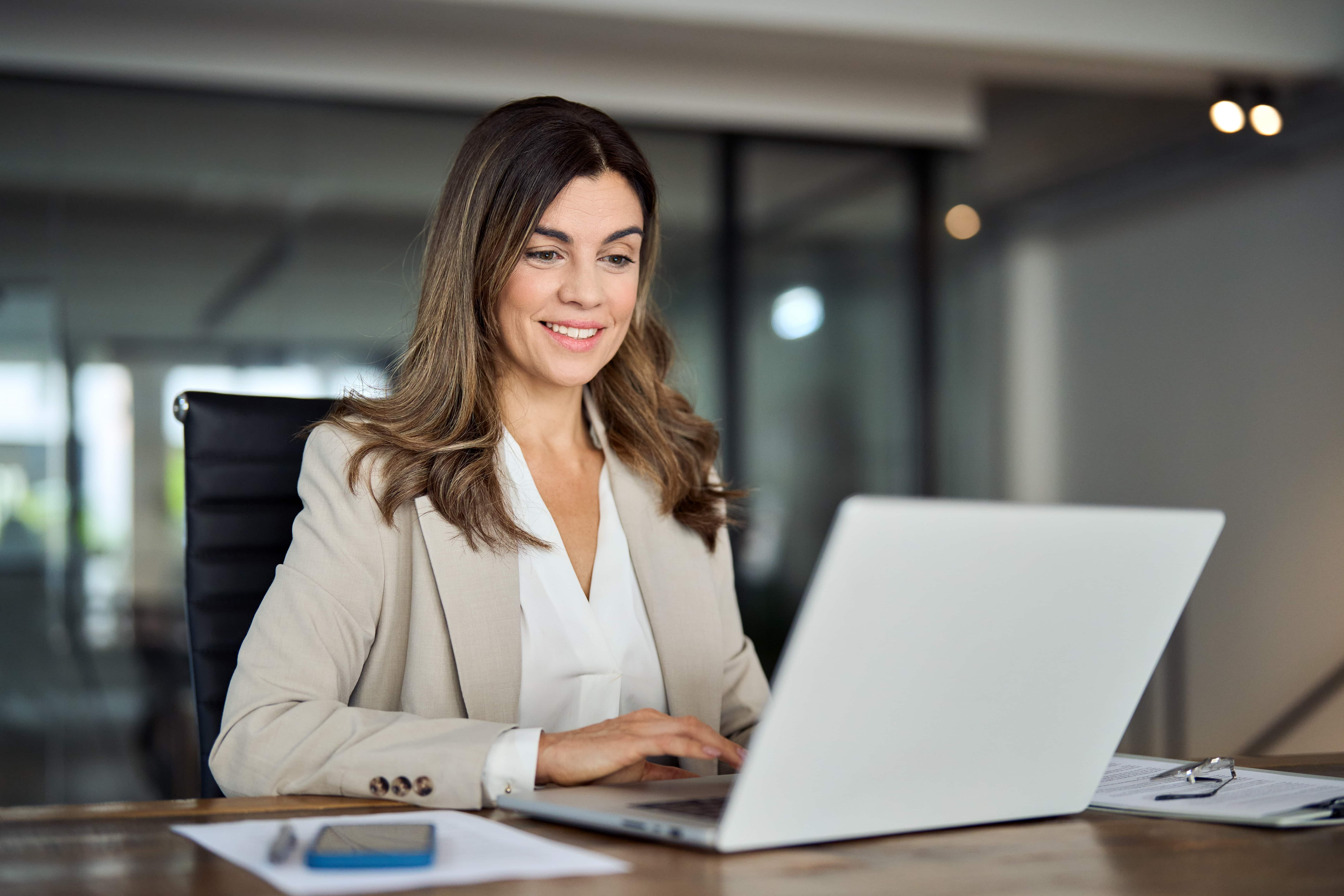 smiling woman in professional attire looking at her laptop